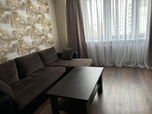 Комната с тёмным диваном, винтажными обоями, кофейным столиком и видом на высотки за окном.