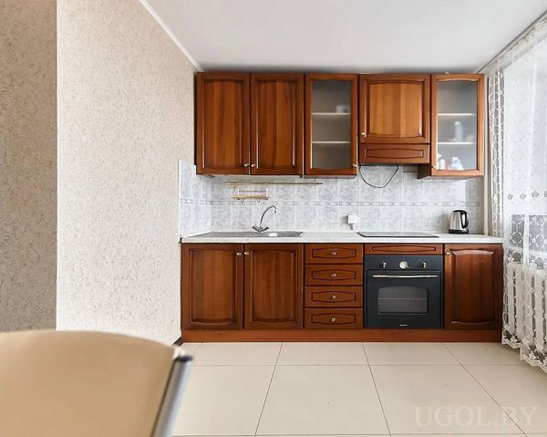 Кухня с деревянными шкафами, белой столешницей, плиткой на фартуке и электрической духовкой.