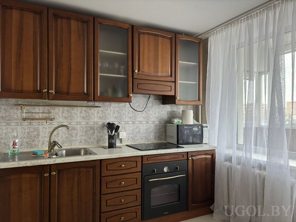 Функциональная кухня с деревянными фасадами, плитой, микроволновкой и фартуком в серых тонах.