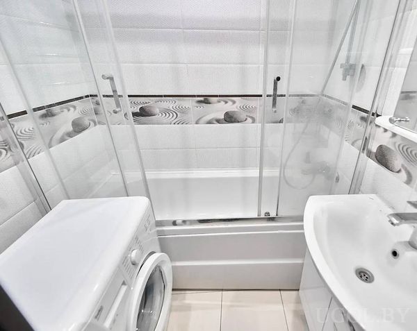 Компактная ванная с стиральной машиной, ванной за стеклом и фартуком с узором из камней и песка.