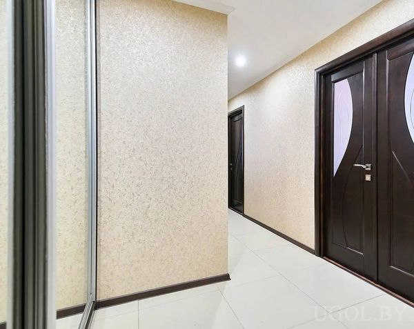 Чистый коридор с белыми плитами, тёмными дверями с матовым стеклом и зеркальным шкафом.