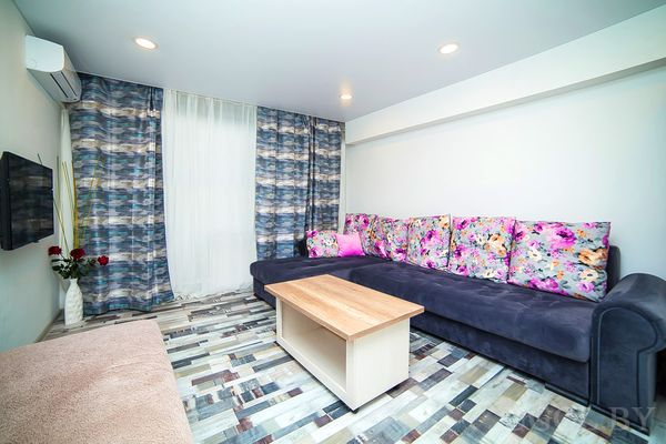 Комната с диваном, столом, телевизором, вазой, тюлем, плиткой и кондиционером.