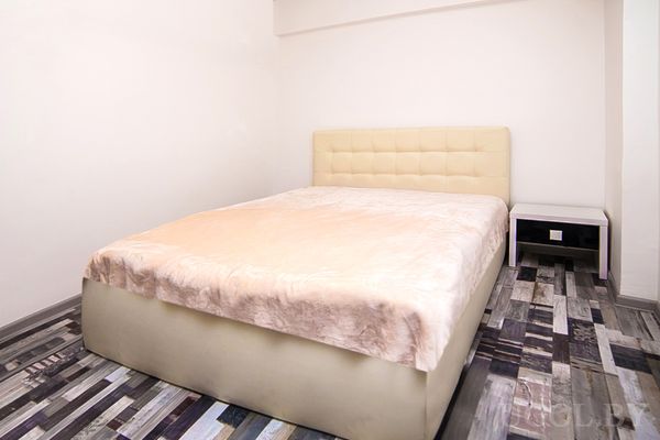 Интерьер с кроватью, тумбой, деревянным полом и белыми стенами.