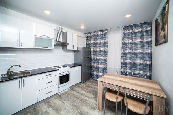 Рабочая зона с плитой, вытяжкой, холодильником, столом, шторами и картиной.