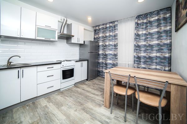 Кухня с плитой, вытяжкой, холодильником, столом, шторами и картиной.