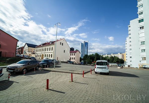 Уличная сцена с высотками, дорогой, машинами, деревьями и облачным небом.