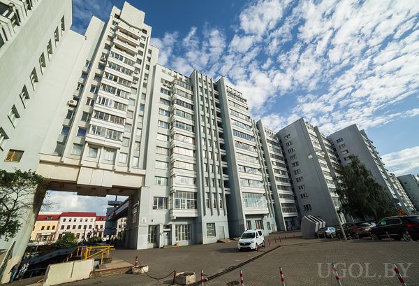 Городская сцена с высотками, аркой, машинами и облачным небом.