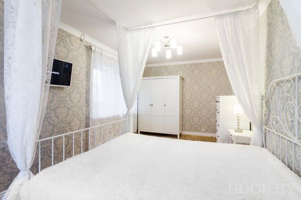 Интерьер с кроватью, балдахином, шкафом, тумбой, светильником, телевизором и нейтральной отделкой.