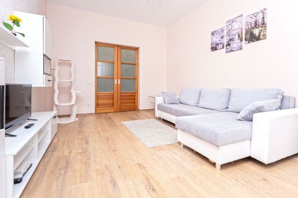 Светлая гостиная с серо‑белым угловым диваном, телевизором на тумбе, когтеточкой для кошки и тремя пейзажами над диваном.