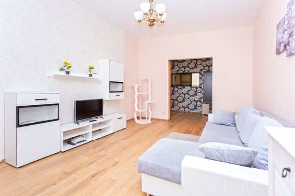 Современная гостиная с серым угловым диваном, телевизором, белой тумбой, зелёными растениями и когтеточкой для кошки.