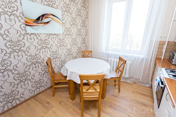 Небольшая кухня с круглым столом, белыми шкафами, плитой и стеной с узорчатыми обоями.