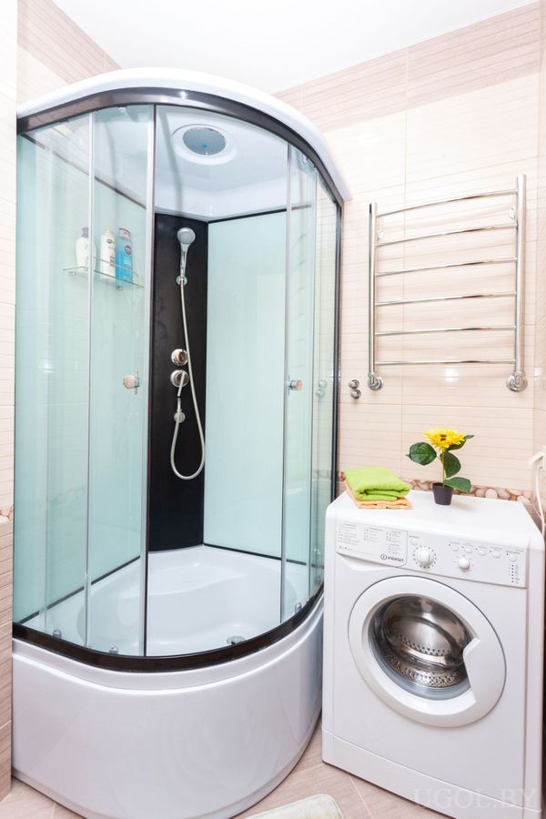 Компактная ванная с душевой кабиной, стиральной машиной, полотенцесушителем и жёлтыми цветами в вазе.