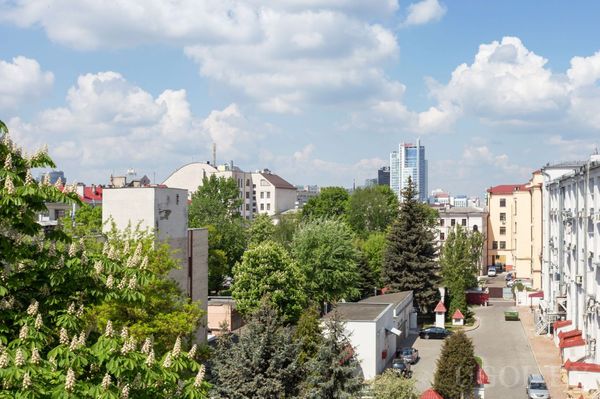 Городской пейзаж с жилыми домами, деревьями и современными небоскрёбами на фоне.