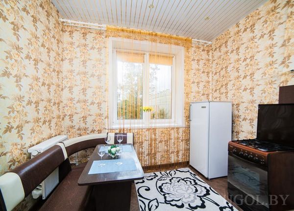 Небольшая кухня с цветочными обоями, угловым диванчиком, накрытым столом, плитой и холодильником.