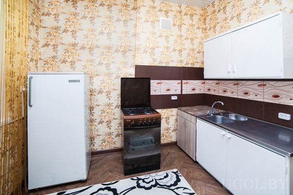 Небольшая кухня с ретро‑обоями, плитой, холодильником, мойкой и белыми шкафами.