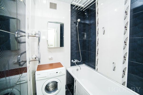 Современная ванная с белой ванной, стиральной машиной, зеркальным шкафчиком и плиткой в синих и белых тонах.