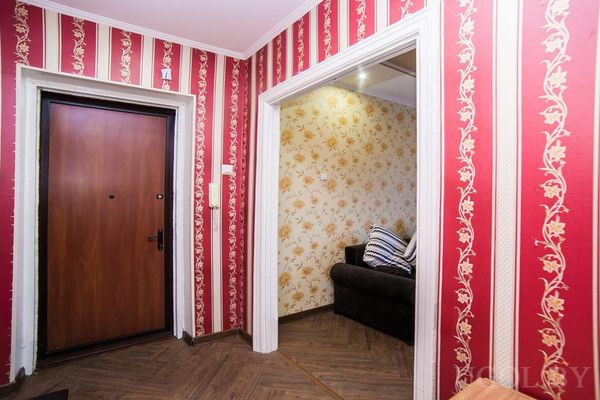 Прихожая с красными обоями в полоску, деревянным полом и дверью, ведущей в комнату с жёлтыми обоями.