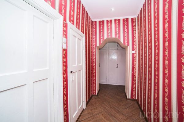 Коридор с красно‑белыми обоями в полоску, деревянным полом и арочным проёмом с белыми дверями.