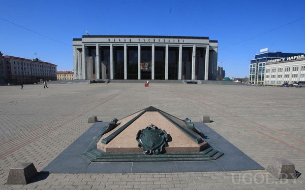 Большая городская площадь с Дворцом Республики в классическом стиле на фоне и декоративным гербом в мощёном покрытии.