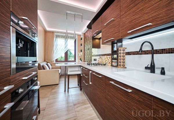 Тёмные фасады, белая столешница, встроенная техника и стол у окна с видом на гостиную.