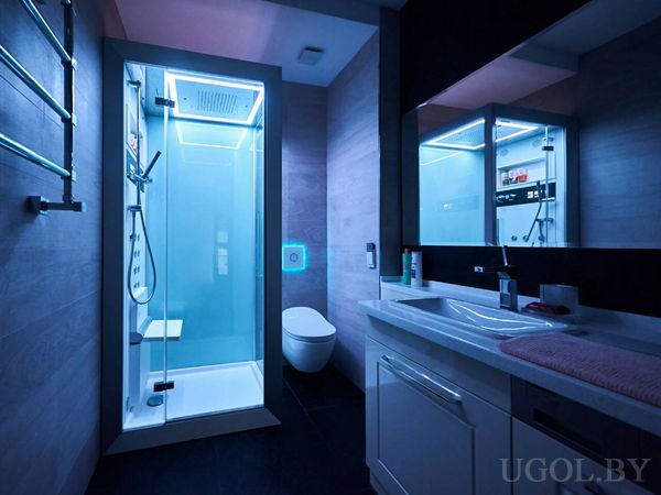 Душевая кабина с подсветкой, подвесной унитаз и зеркало с отражением, интерьер в холодных тонах.