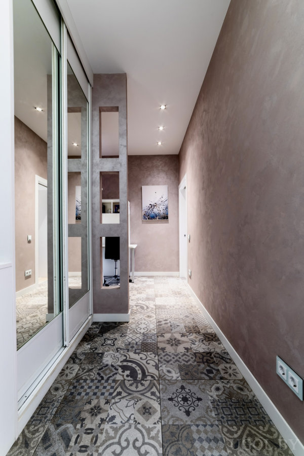 Коридор с плиткой, зеркальной дверью, перегородкой с нишами и картиной на фоне мягкой отделки.