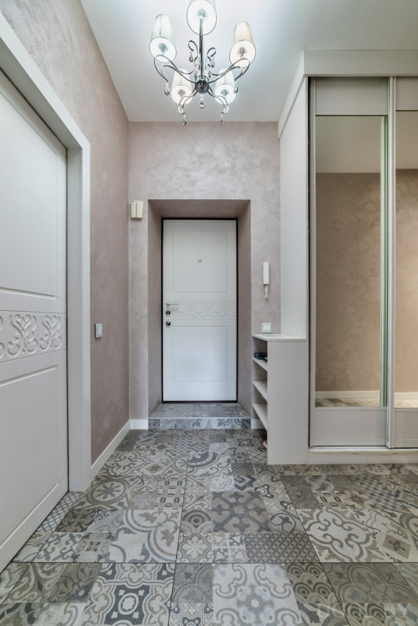 Белая дверь, плитка с орнаментом, зеркальный шкаф и люстра в светлом и элегантном интерьере.