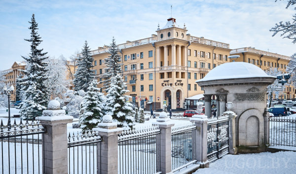 Историческое здание с колоннами и симметричным фасадом на фоне заснеженных деревьев и кованого забора.