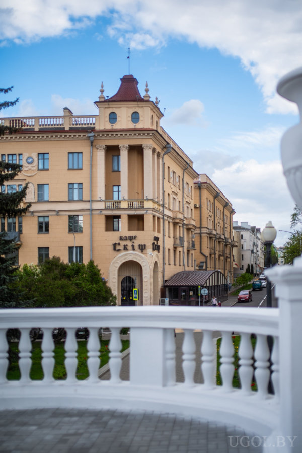 Бежевое здание с колоннами и красной башней, вывеска «кафе Скіф», балюстрада и городская жизнь на фоне.