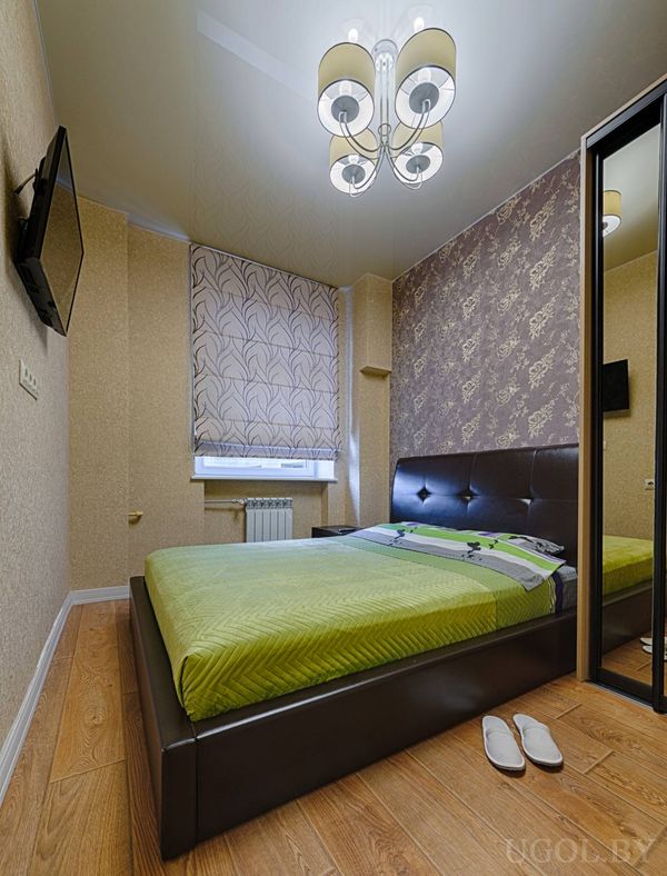 Кровать с тёмным изголовьем, зелёное покрывало, зеркальный шкаф, ТВ и цветочная акцентная стена.