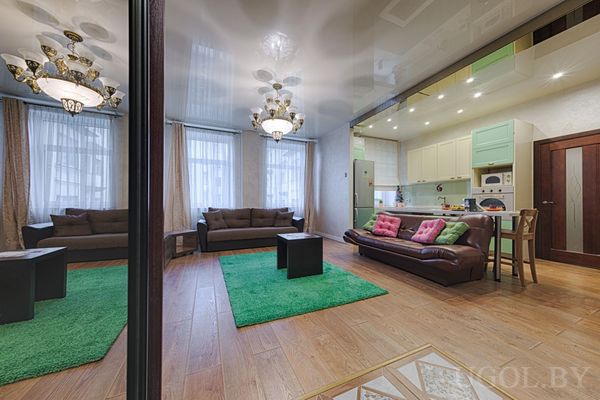 Кровать с кожаным основанием, зелёный текстиль, белые тапочки, зеркальный шкаф и роллет на окне.