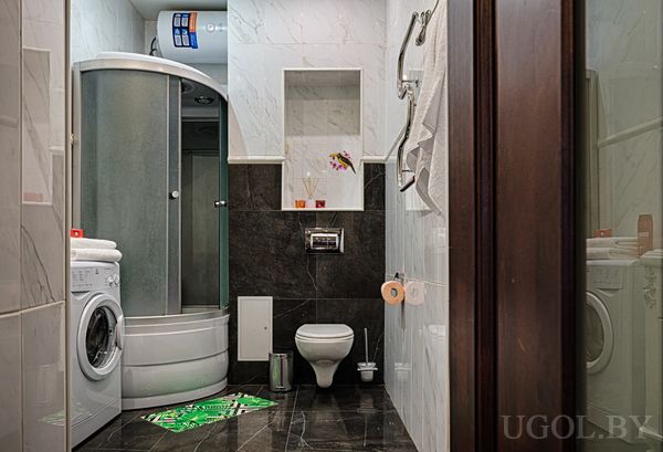Компактная ванная с душевой кабиной, стиральной машиной, настенным унитазом и мраморной отделкой.