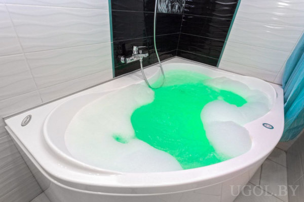 Угловая ванна с ярко-зелёной водой, белая пена, чёрно-белая плитка и настенный душ.