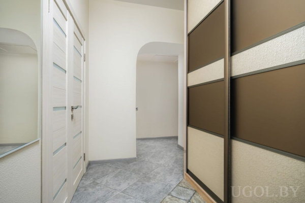 Светлый коридор с арочным проходом, белая дверь с матовыми вставками и шкаф с бежево-коричневыми панелями.