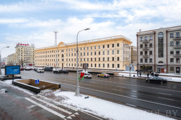 Здание классической архитектуры, пятиэтажный фасад, широкая дорога с машинами и зимний пейзаж.