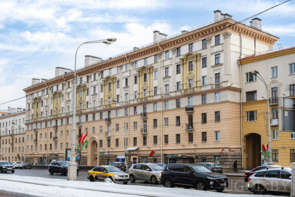 Классический фасад с колоннами и декоративными элементами, дорога со снегом, машины и национальные флаги.