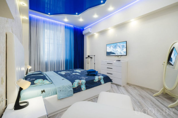 Современная спальня с зеркалом в полный рост, кондиционером и телевизором с горным пейзажем.