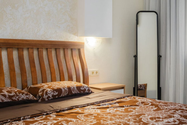 Тёплая спальня с деревянной кроватью, орнаментальным текстилем и высоким зеркалом.