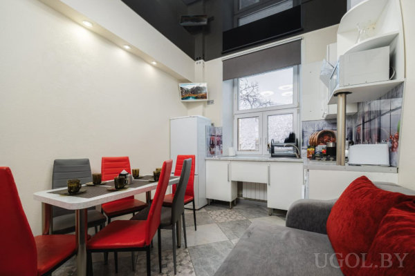 Компактная кухня с белыми шкафами, плиткой и красными элементами в интерьере.