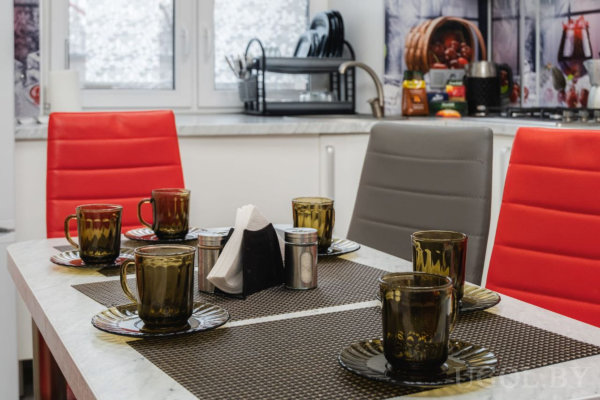 Обеденный стол с чашками, салфетками и современными красно-серыми стульями.