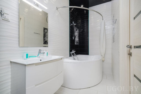 Современная ванная с угловой ванной, белой мебелью и контрастной плиткой с изображением женщины.