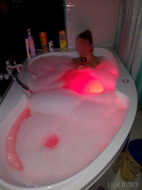 Человек в ванной с пеной и бокалом, в атмосфере красной подсветки и личных принадлежностей.