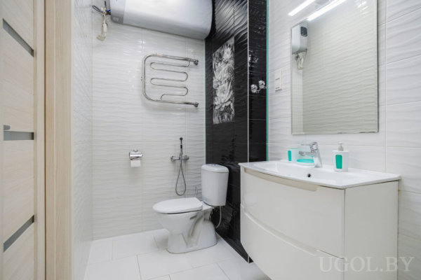 Минималистичная ванная с белой сантехникой, зеркалом и настенным водонагревателем.