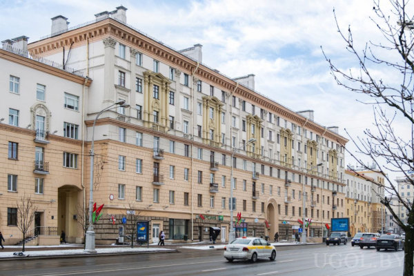 Городская сцена с классическим зданием, магазинами и мокрой дорогой.