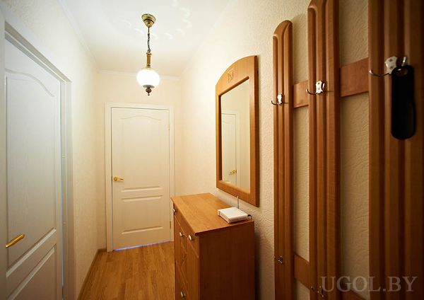 Узкий коридор, деревянная мебель, зеркало, светильник, белые двери, акцент на порядок и светлую отделку.