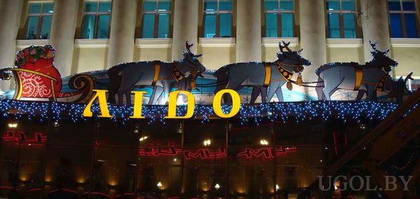 Олени и сани на фоне колонн, гирлянды, праздничная атмосфера, акцент на бренд и сезонное оформление.