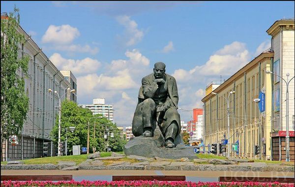 Центральная скульптура, цветы у постамента, архитектура вокруг, дневной свет, культурный ориентир Минска.