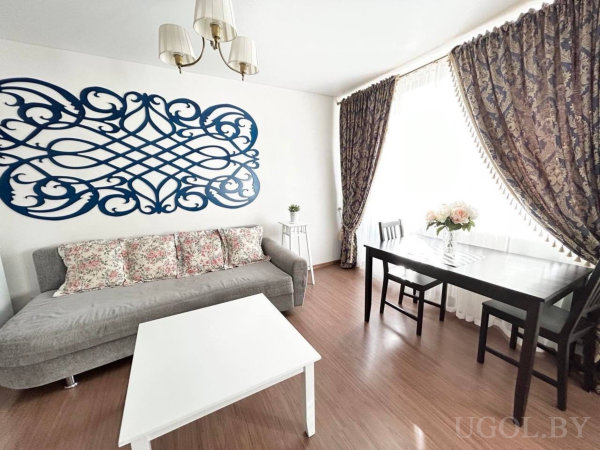 Интерьер с диваном, столом, цветами, синим настенным орнаментом и шторами с узором.