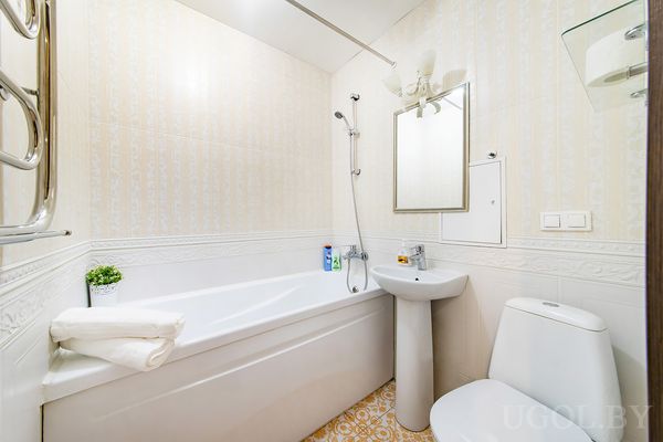 Комната с ванной, умывальником, унитазом, зеркалом, светильником и декоративной плиткой.