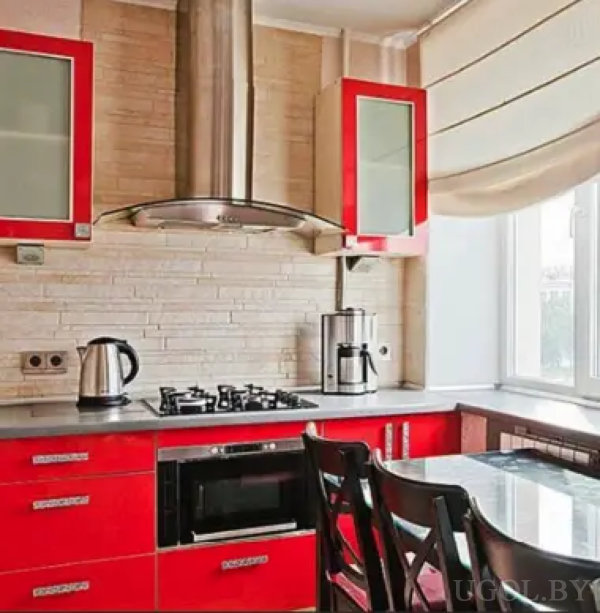 Современная кухня с красными шкафами, плиткой под кирпич, газовой плитой и стеклянным обеденным столом. Пространство наполнено светом благодаря большому окну с римской шторой.